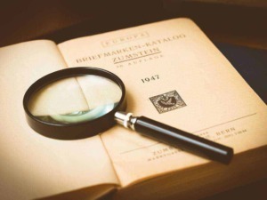 Libro antico aperto con lente d'ingrandimento su pagina, esplorazione storica e archivio documentale, focus su volumi di valore e ricerche approfondite.