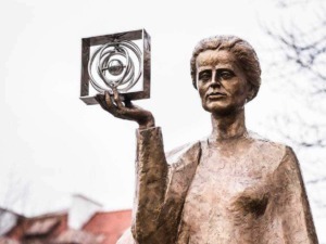 Estatua di una donna con il braccio alzato che tiene un oggetto artistico in metallo, simbolo di creatività e cultura.