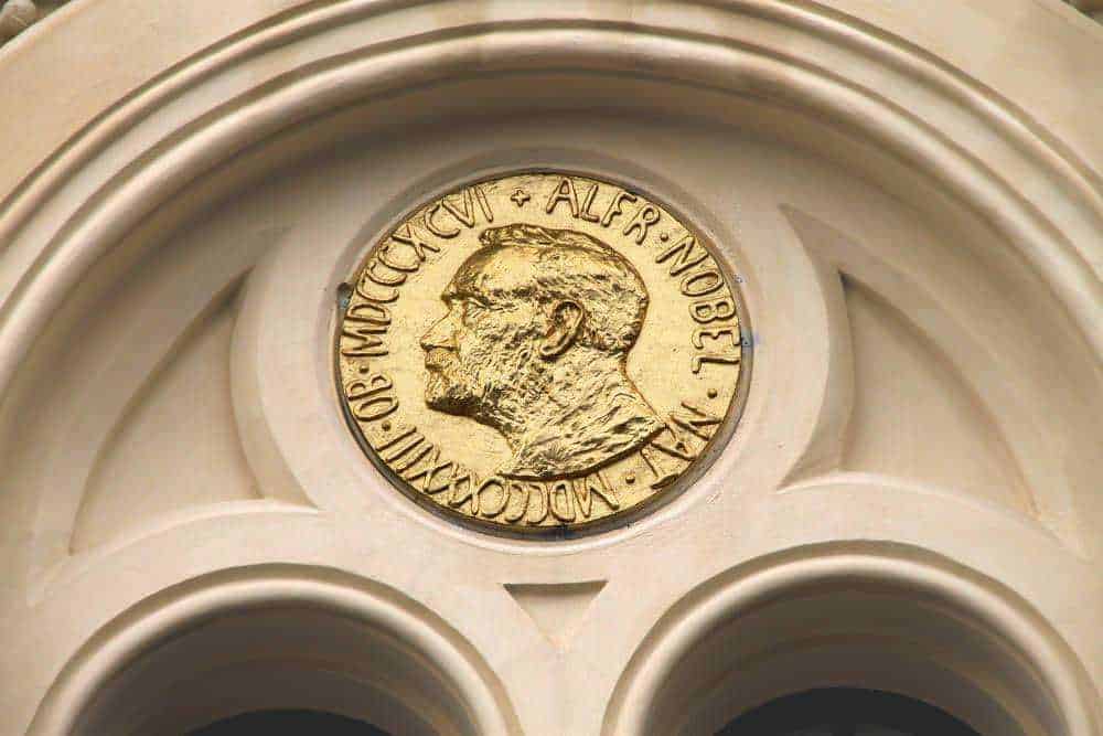 Moneta d'oro con profilo di una figura storica, incisa con precisione e dettagli artistici, incastonata in un dettaglio architettonico classico, simbolo di valore storico e culturale.