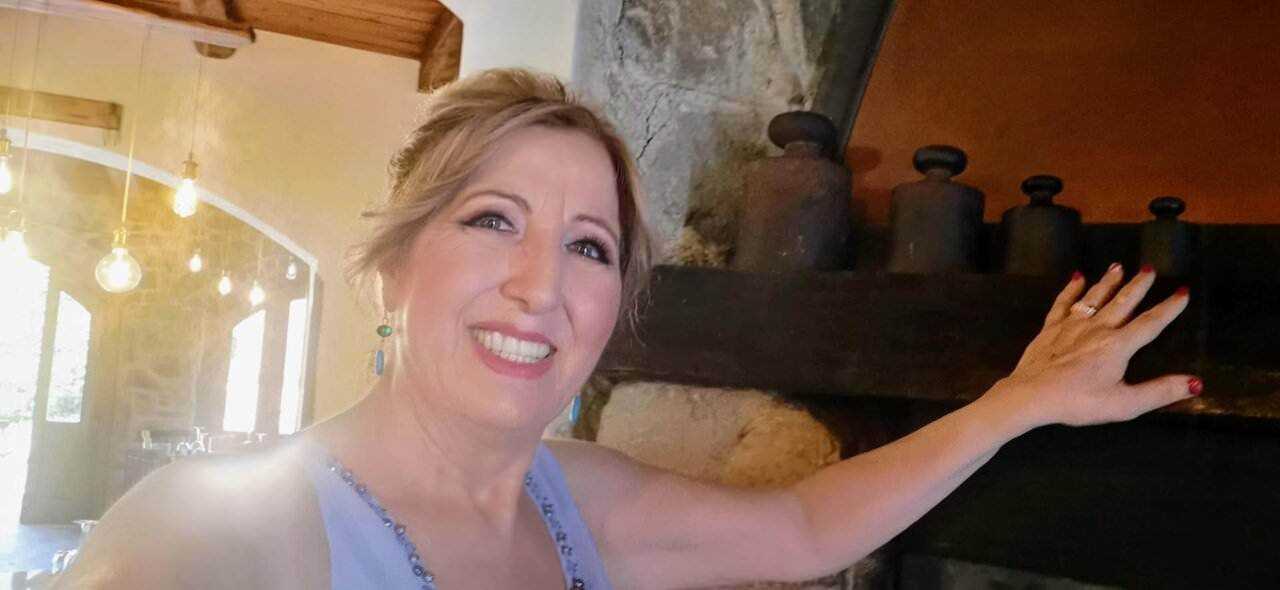 Appunti Sul Blog, immagine di una donna sorridente che si appoggia a una pietra nel soggiorno di una casa rustica con camino, atmosfera calda e accogliente.