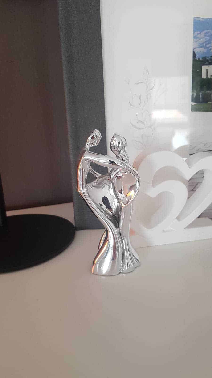 Elegante statua femminile in metallo lucido, decorazione moderna per ambienti living, riflessi di luce sulla superficie cromata.