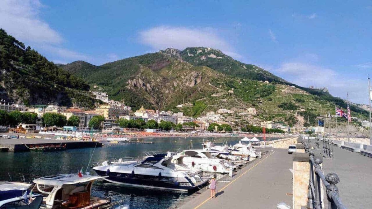 Barche a vela ormegiate nel porto di Amalfi con un pittoresco paesaggio montano sullo sfondo, idealmente situato sulla costiera amalfitana, perfetto per viaggi e vacanze in Italia.