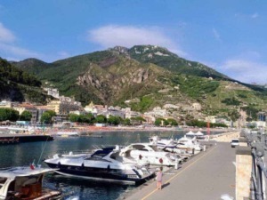 Barche a vela ormegiate nel porto di Amalfi con un pittoresco paesaggio montano sullo sfondo, idealmente situato sulla costiera amalfitana, perfetto per viaggi e vacanze in Italia.