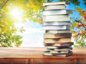 Pila di libri su un tavolo di legno con sfondo di alberi in autunno e cielo soleggiato.