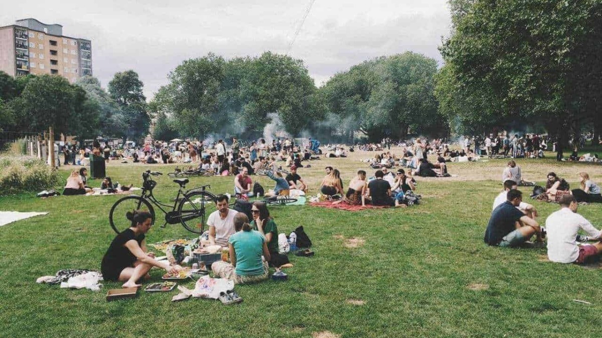 Sosta al parco con gruppi di persone che fanno picnic e socializzano sotto grandi alberi, con grigliate e biciclette parcheggiate.