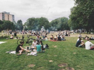 Sosta al parco con gruppi di persone che fanno picnic e socializzano sotto grandi alberi, con grigliate e biciclette parcheggiate.