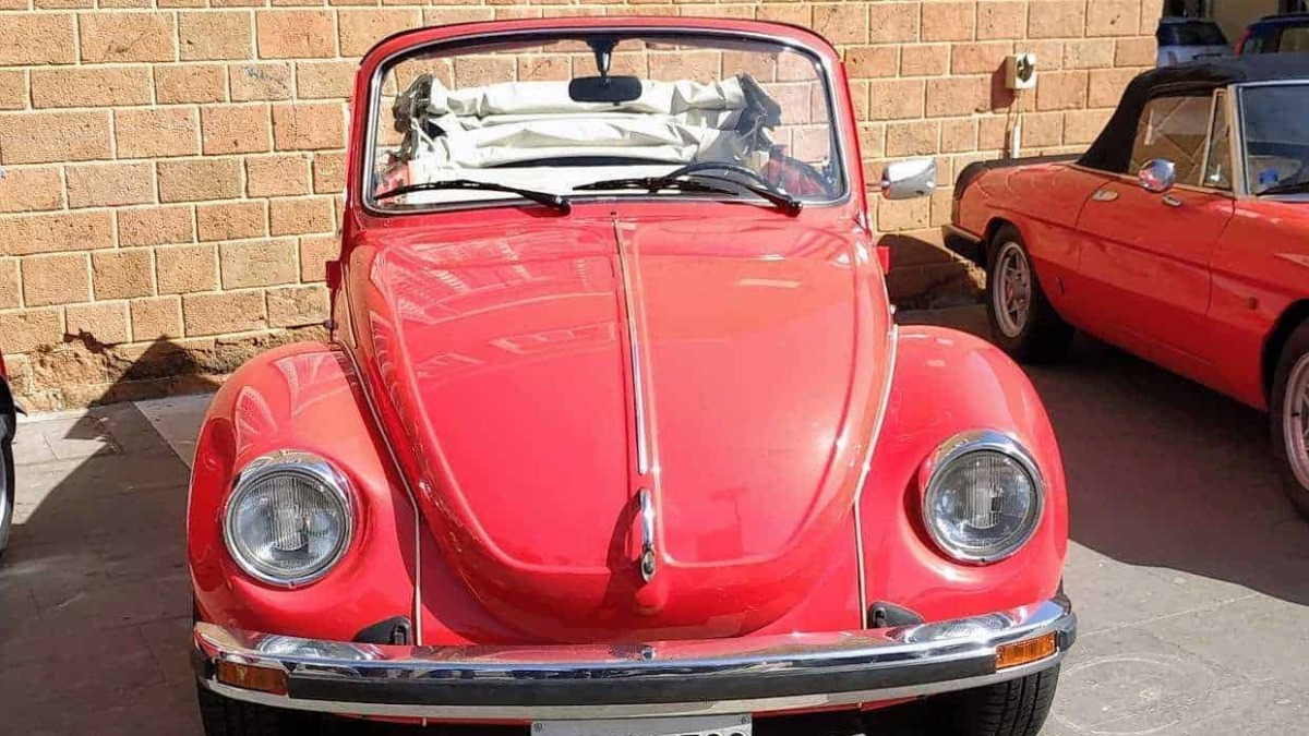 Volkswagen Maggiolino rossa d'epoca in esposizione di fronte a una parete di mattoni.