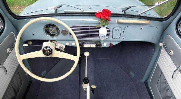 Volante vintage e cruscotto d'epoca all’interno di un’auto classica, decorata con fiore rosso in vaso sulla plancia, ambiente retrò e affascinante, perfetto per appassionati di automobili d’epoca e design vintage.