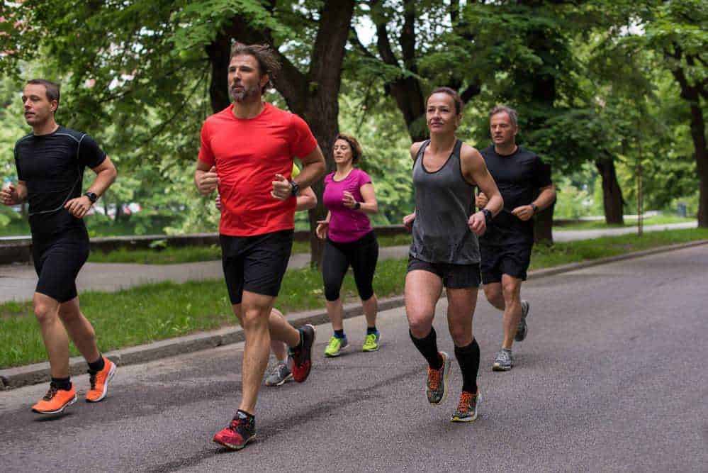 Allenamento di corsa all'aperto in parco con un gruppo di persone che praticano jogging per migliorare salute e benessere. Gruppo di runners che si allenano durante una passeggiata in natura.