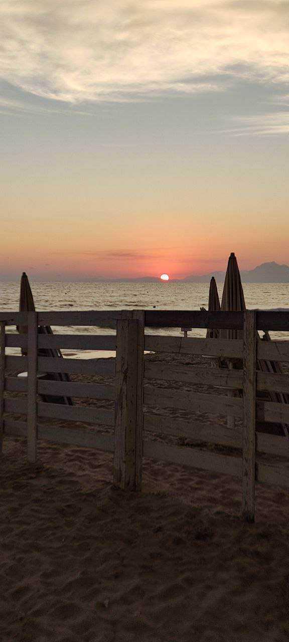 Cosa vedere nel parco del Cilento e Vallo di Diano 3 Tramonto sulla spiaggia con ombrelloni e rete in legno, atmosfera tranquilla e rilassante, perfetta per vacanze estive, lontano dal caos urbano.