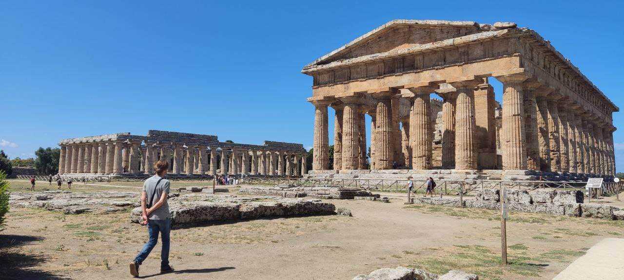Cosa vedere nel parco del Cilento e Vallo di Diano 2 Maestoso tempio greco antico con colonne doriche, sito archeologico in Grecia, visitatori scoprono la storia dell'antica civiltà, cielo azzurro e sole splendente illuminano le rovine.
