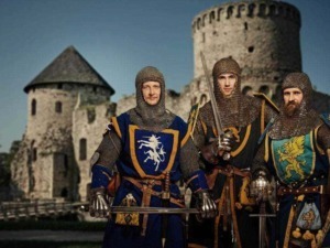 Swordsmanship medieval knights in armor and helmets with colorful heraldic shields standing in front of a historic stone castle during daytime.