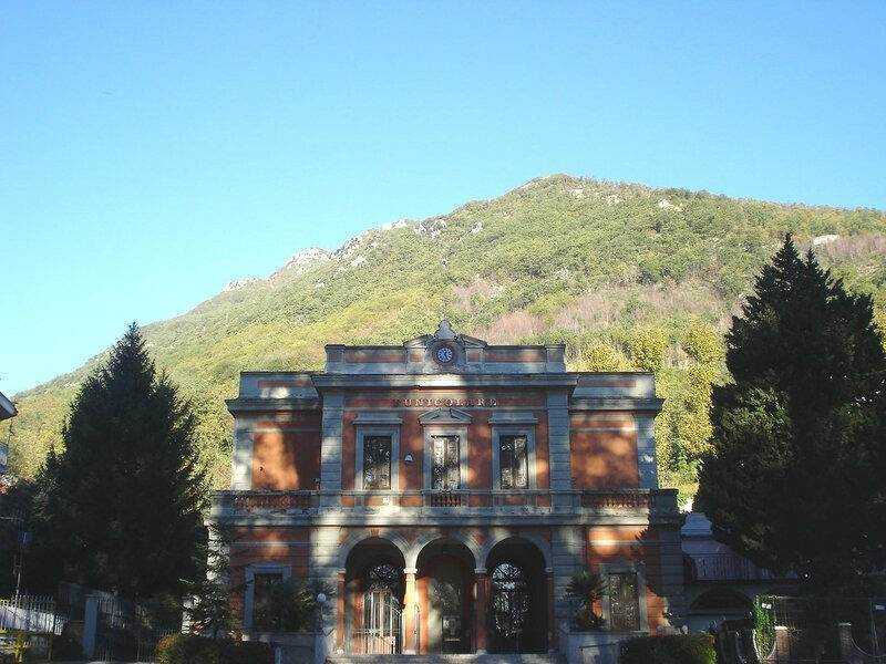 Antica stazione ferroviaria in stile classico con archi e dettagli in pietra, immersa nel contesto naturale delle montagne verdi e alberi carreggiati, in un paesaggio di tranquillità e storia.