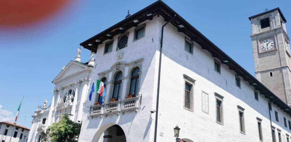 Palazzo storico con torre dell'orologio e bandiere italiane e europee, esempio di architettura tradizionale italiana a Belluno, Veneto, città con ricca storia e patrimonio culturale.