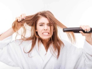 Brava donna arrabbiata che si piastra i capelli, frustrata durante la luminosità del giorno. Donna in vestaglia bianca che si appresta a sistemare i capelli con frustrante esperienza di stile.