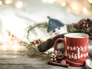 Tazza di cioccolata calda con dedica natalizia, decorata con elementi di Natale come pigne, corteccia di canna e pupazzo di neve di lana, atmosfera festiva e calda per le festività natalizie.