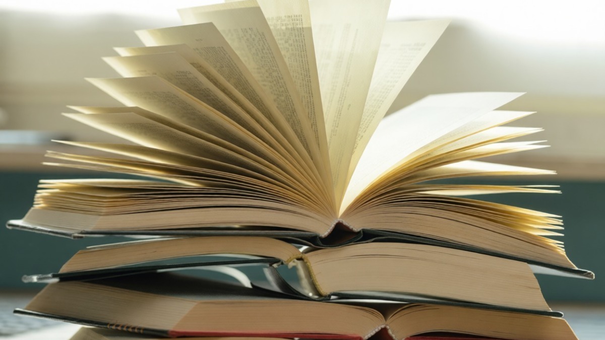 Vecchi libri impilati con uno di essi aperto e volto verso l'alto, rappresentando la lettura e lo studio.