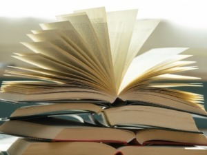 Vecchi libri impilati con uno di essi aperto e volto verso l'alto, rappresentando la lettura e lo studio.
