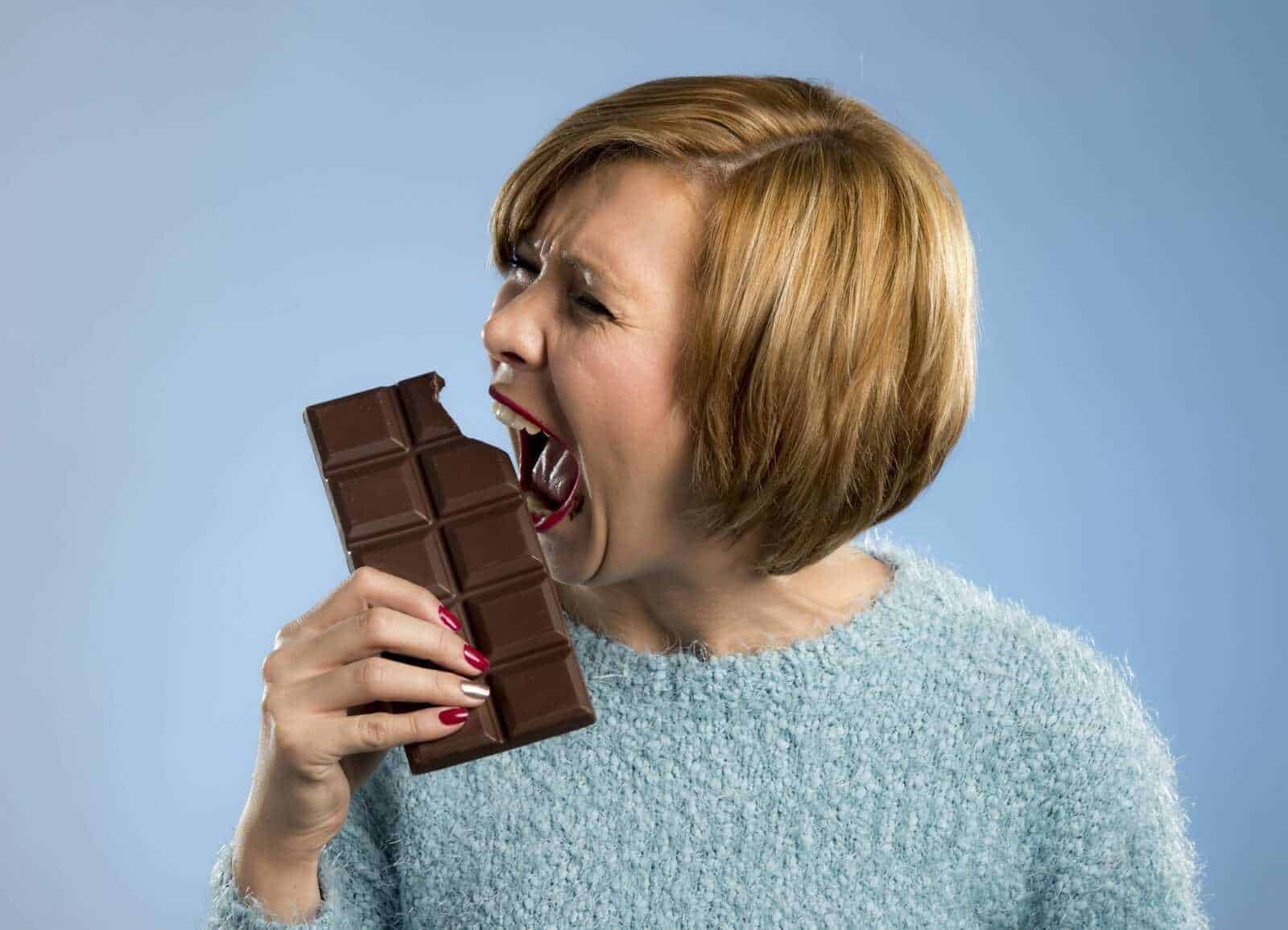 12 benefici associati al cioccolato fondente 3 Barretta di cioccolato fondente mangiata da una donna con bocca aperta, emozione di golosità e tentazione, immagine di dolci e cioccolato, perfetta per blog di ricette e lifestyle dolci.