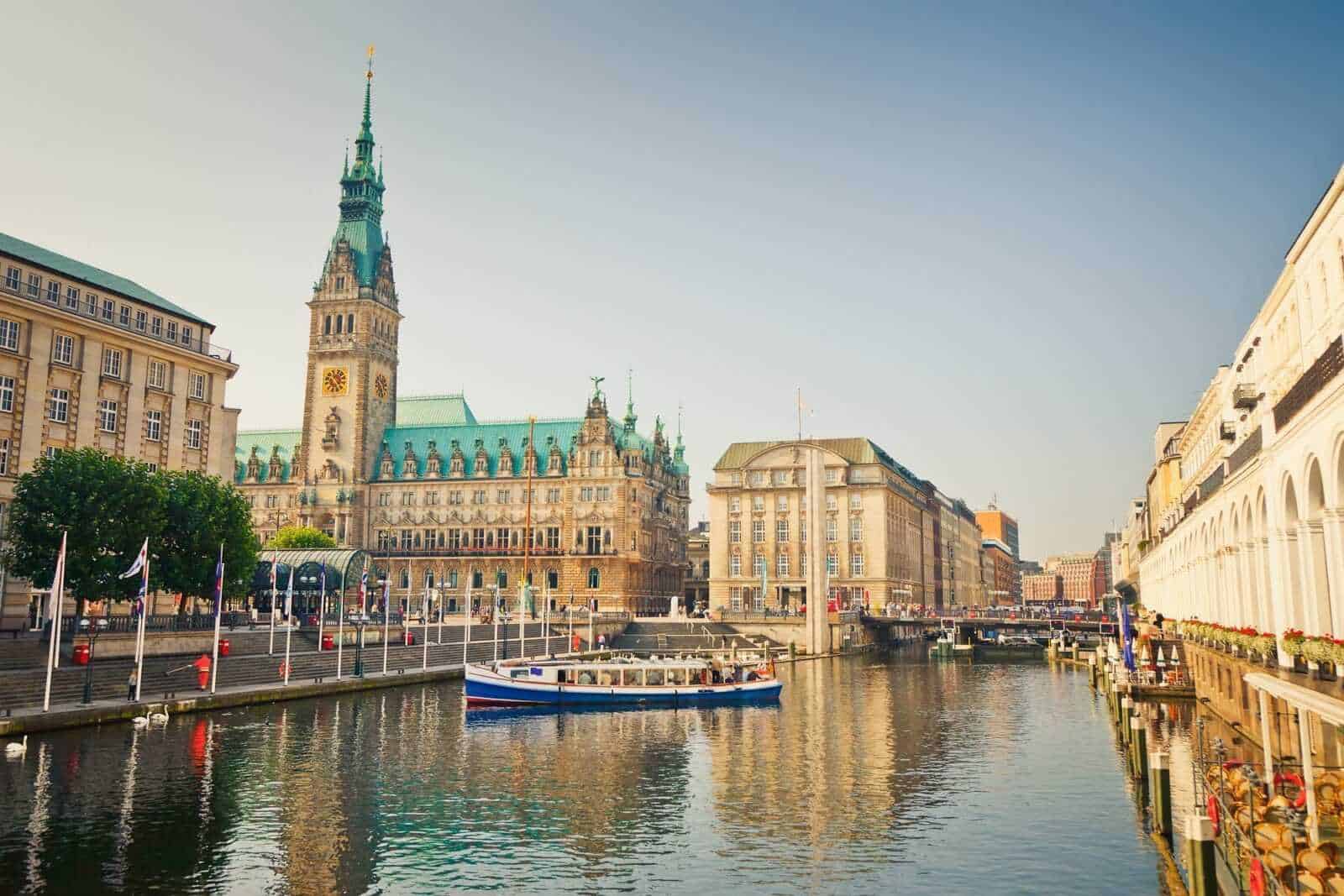 13 Città con canali nel mondo da vedere 11 Palazzo del Municipio di Hamburgo con il suo campanile storico, vista sul porto e il fiume Alster, in una giornata di sole senza nuvole, tra edifici storici e moderni.