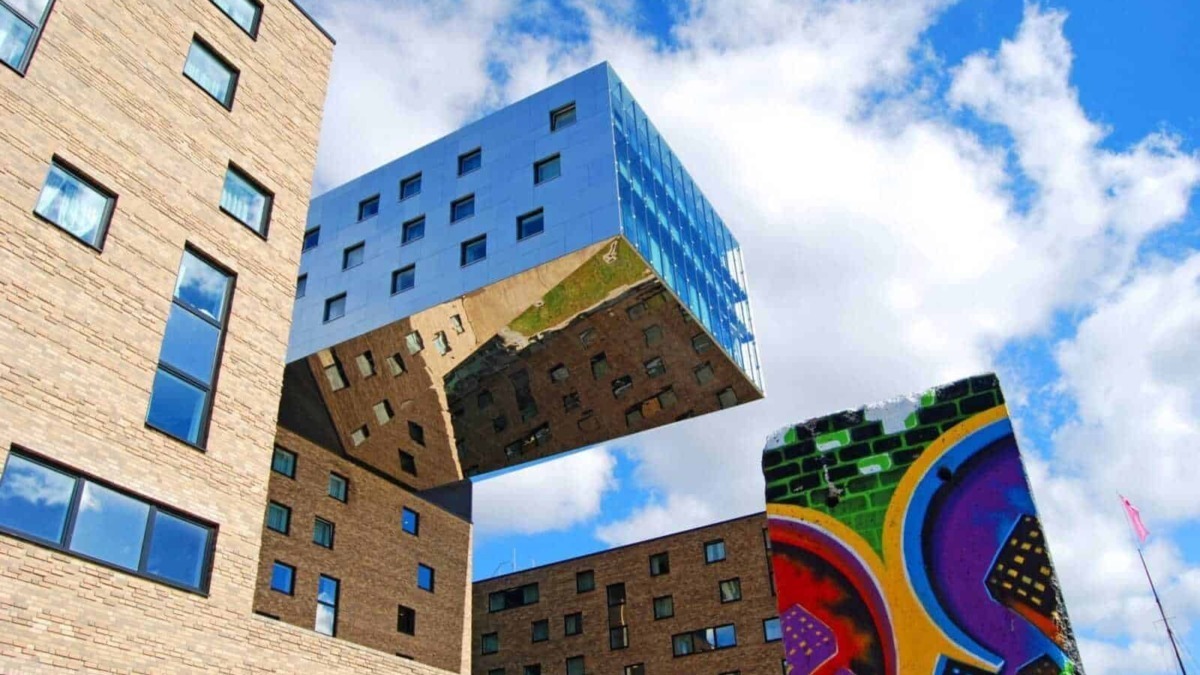 Grattacielo con facciata in vetro riflettente, architettura moderna e murales colorati, sotto un cielo sereno con nuvole, esempio di design urbano innovativo e arte di strada a cielo aperto.