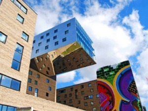 Grattacielo con facciata in vetro riflettente, architettura moderna e murales colorati, sotto un cielo sereno con nuvole, esempio di design urbano innovativo e arte di strada a cielo aperto.