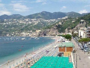 Spiaggia di Sorrento con ombrelloni, mare cristallino e montagne sullo sfondo, ideale per vacanze estive e relax in Italia.