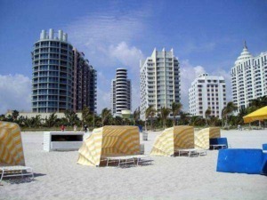 Grattacieli moderni sulla spiaggia di Miami con ombrelloni gialli e lettini, scenario di una costa turistica americana, ideale per foto di viaggi e vacanze al mare.