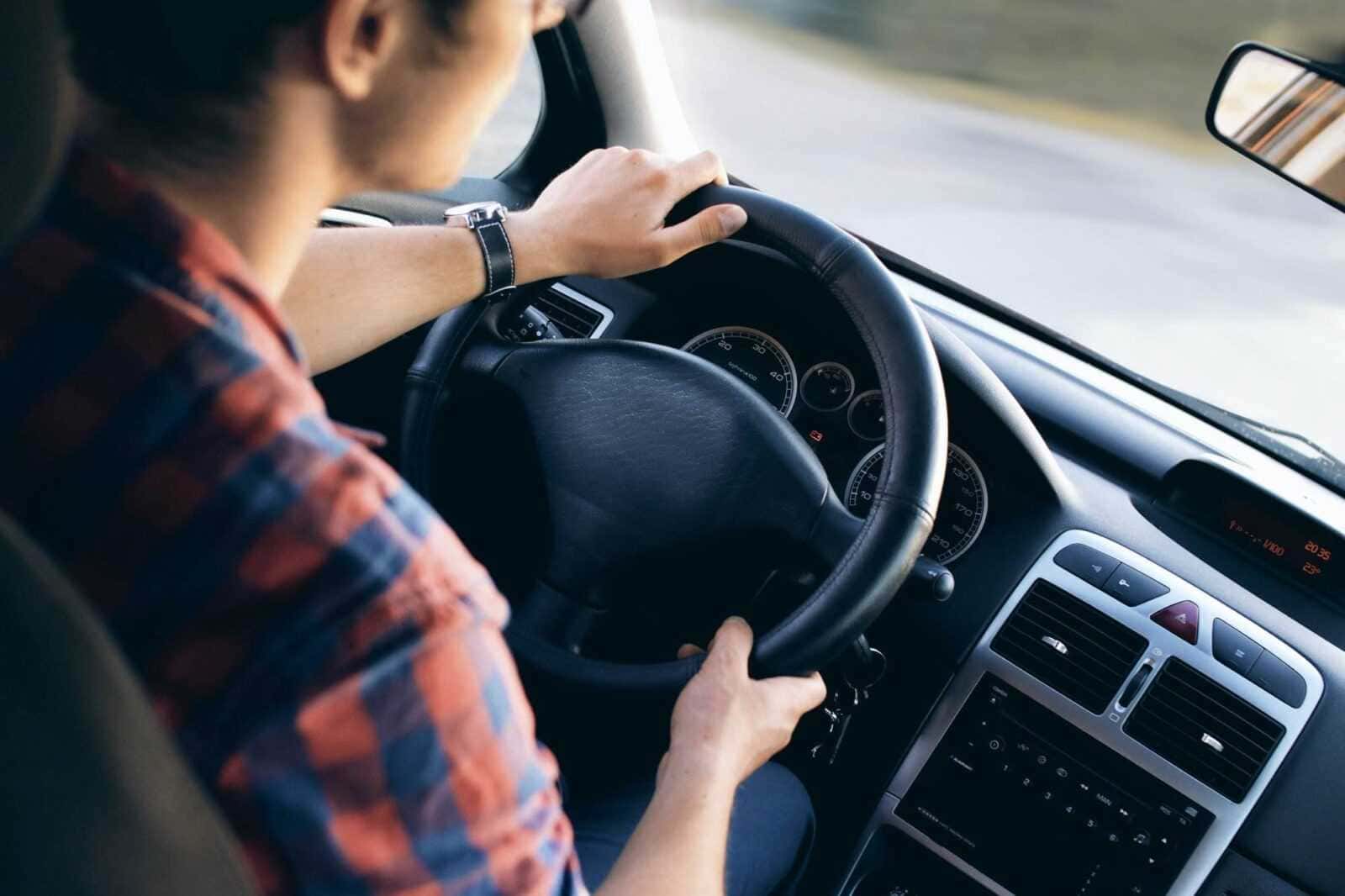 Guidatore con camicia a quadri che tiene il volante dell'auto, vista da dietro, durante un viaggio su strada.