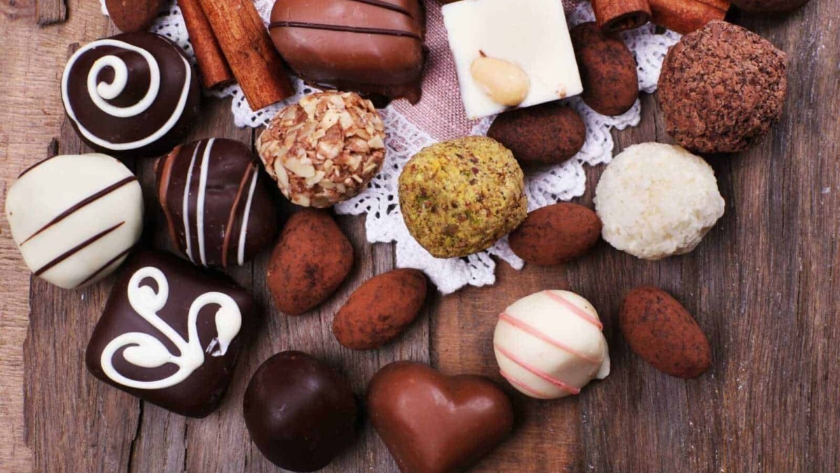 Extravaganza di praline e cioccolatini artigianali decorati, assortiti e appetitosi su tavola di legno rustica, perfetti come dolciumi e regali golosi.