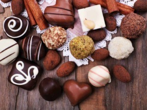 Extravaganza di praline e cioccolatini artigianali decorati, assortiti e appetitosi su tavola di legno rustica, perfetti come dolciumi e regali golosi.