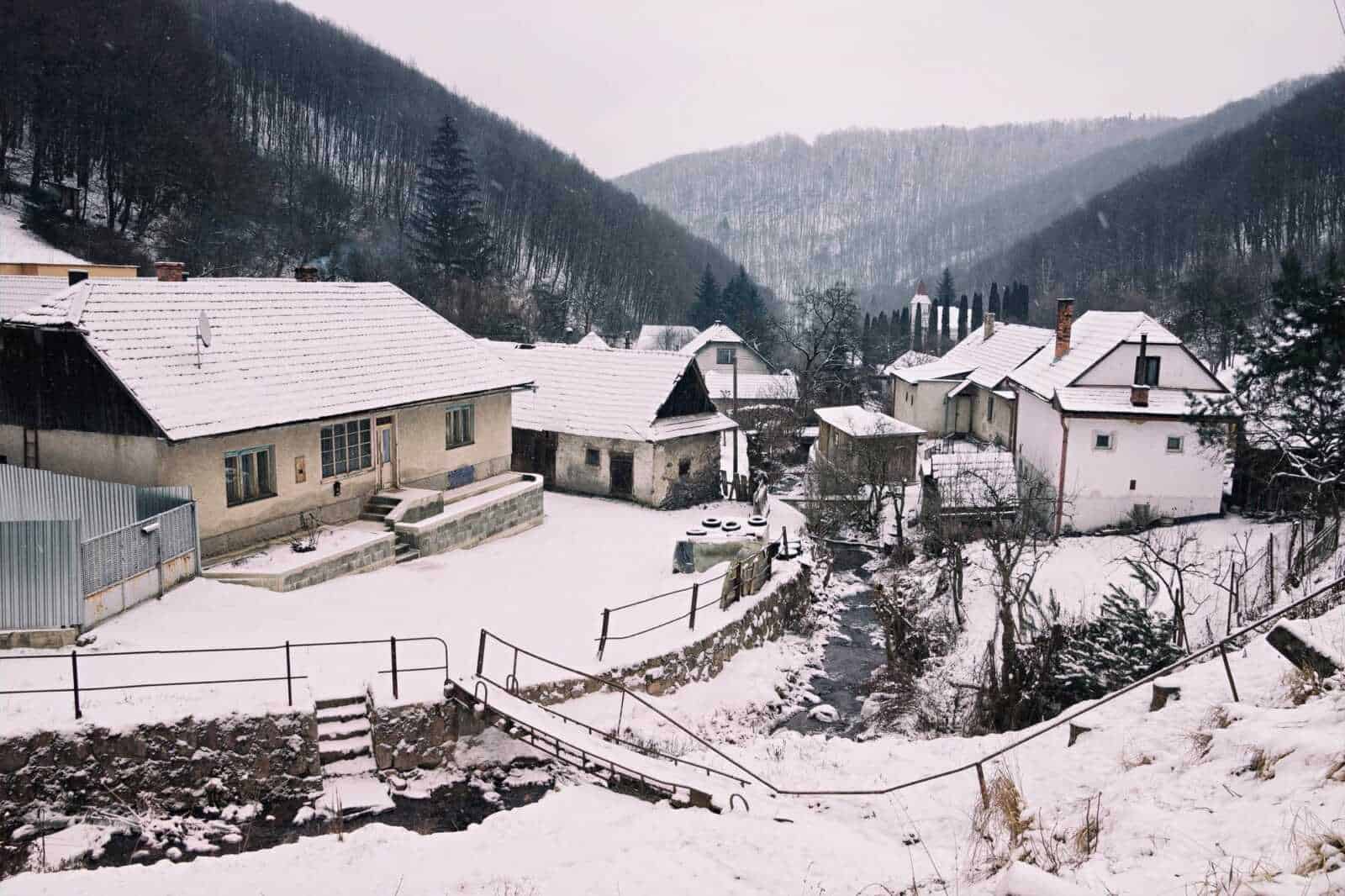 Case di montagna innevate in un paesaggio rurale con boschi e un piccolo corso d'acqua, tutto immerso nella tranquillità della natura invernale in Italia.
