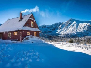 Casetta di legno rossa coperta di neve con montagne innevate sullo sfondo in un paesaggio invernale; luogo ideale per appunti sul blog di viaggio.