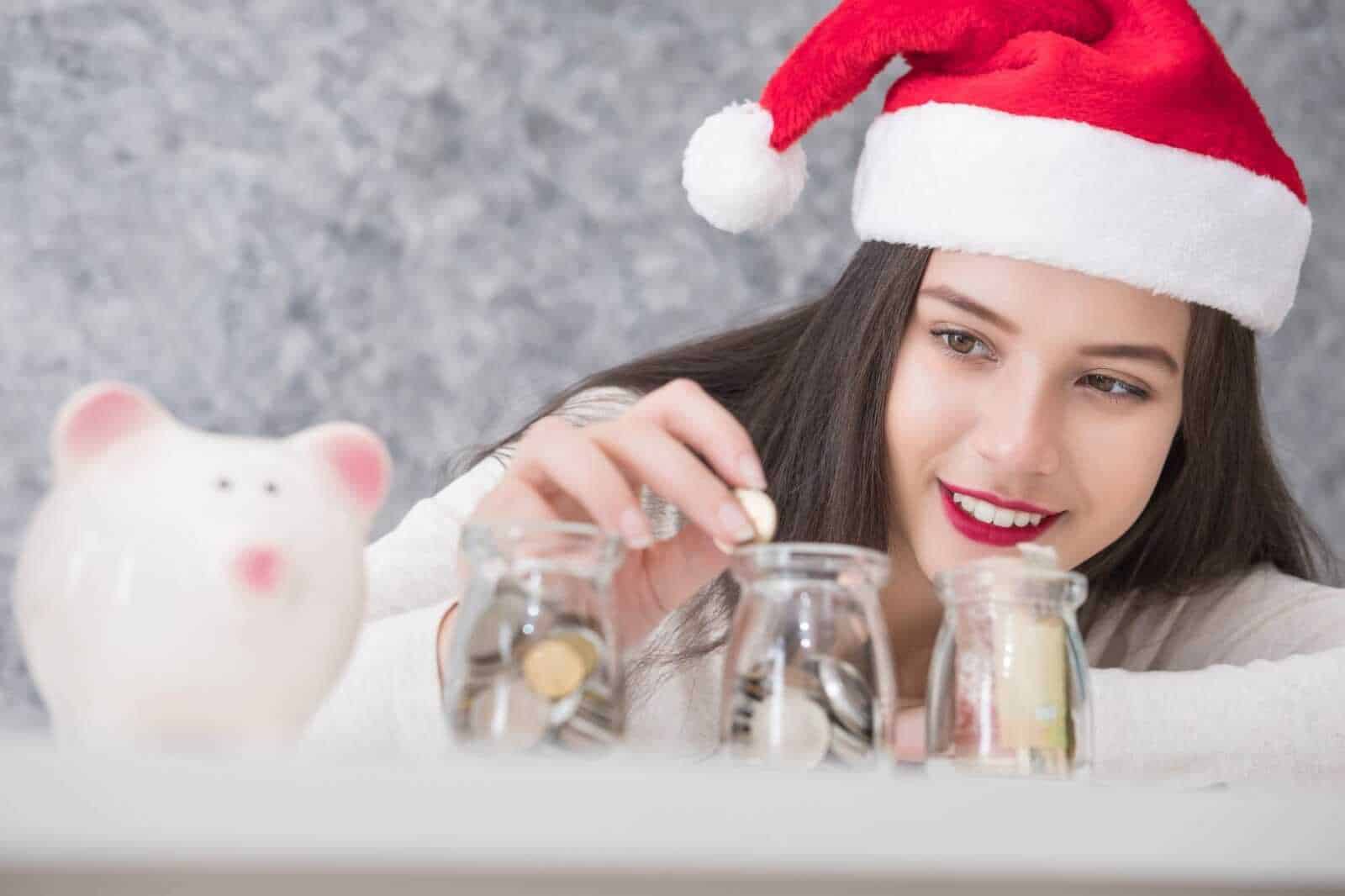 Risparmio natalizio: ragazza con berretto di Babbo Natale, scatole e portamonete, simboli di economia festive.