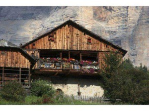 Vecchio chalet in legno con balcone fiorito situato ai piedi di una parete di roccia, immerso nella natura, perfetto per un rifugio montano.