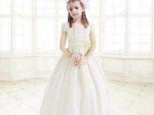 Vestita in abito da cerimonia bianco per bambina, ambiente elegante con grande finestra e lampadario chandelier.