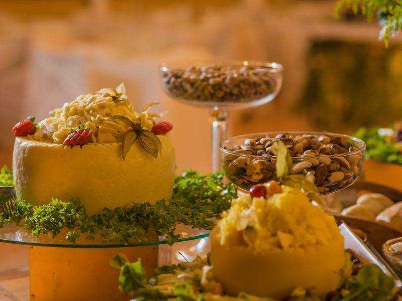 Formaggio decorato con erbe e frutti rossi, servito con nocciole e altri snack in ciotole di vetro, su un buffet di prodotti tipici italiani, perfetto per degustazioni e aperitivi.