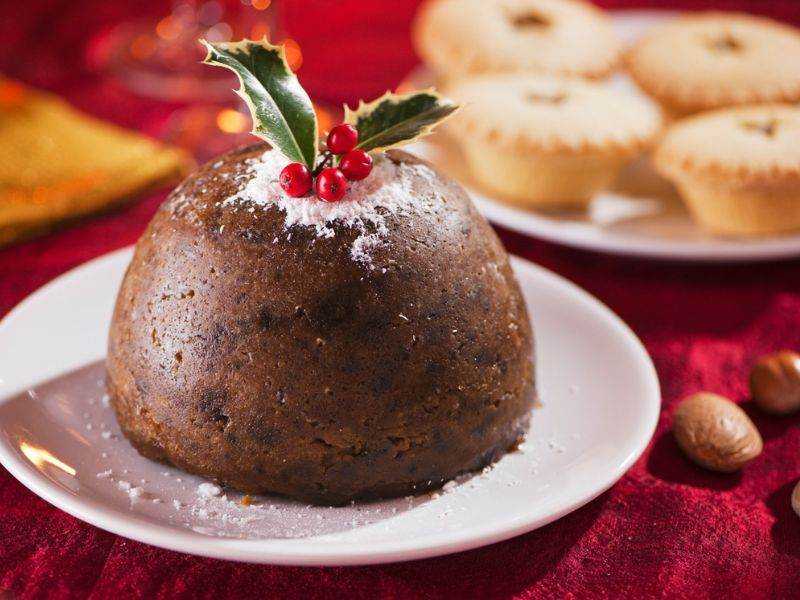 Dolce natalizio al cioccolato con decorazione di agrifoglio e bacche rosse, perfetto per le festività. Presentato su piatto bianco, con biscotti e decorazioni di Natale sullo sfondo.
