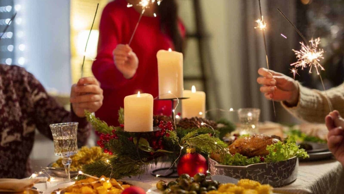 Feste di Natale con candee, persone con scintille, tavola apparecchiata con cibo tradizionale e decorazioni natalizie, atmosfera calda e conviviale.