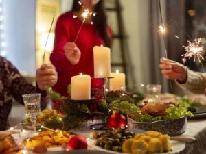 Feste di Natale con candee, persone con scintille, tavola apparecchiata con cibo tradizionale e decorazioni natalizie, atmosfera calda e conviviale.