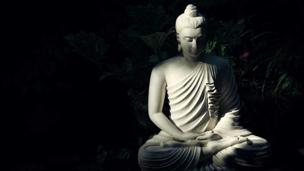 Scultura di Buddha in marmo, illuminata in modo artistico, simbolo di pace e spiritualità, collocata in un giardino zen con piante verdi sullo sfondo.