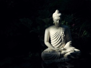 Scultura di Buddha in marmo, illuminata in modo artistico, simbolo di pace e spiritualità, collocata in un giardino zen con piante verdi sullo sfondo.