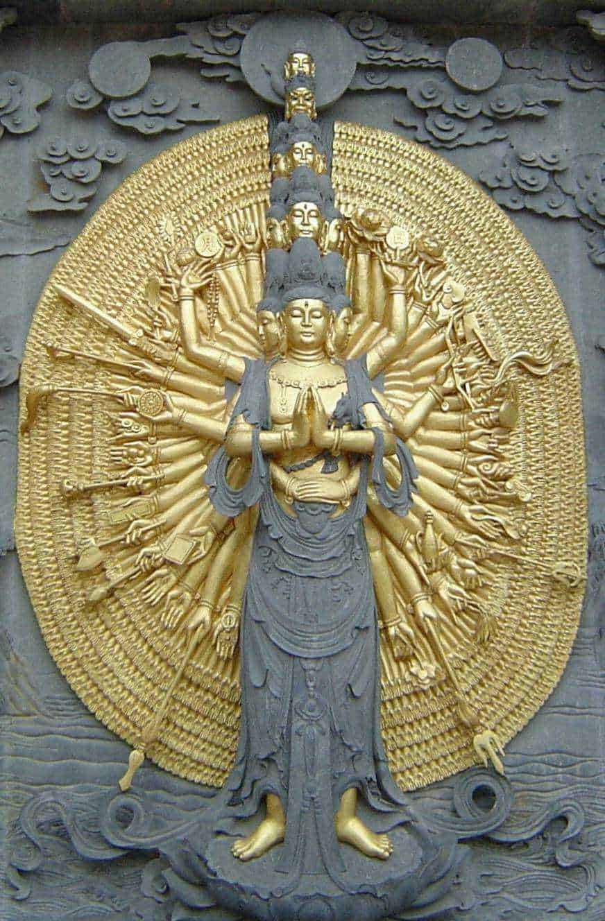 Dettaglio di una statua di Avalokitṣvara, il Bodhisattva della compassione, con molteplici braccia e teste, in stile buddhista asiatico, con superficie dorata e dettagli elaborati.