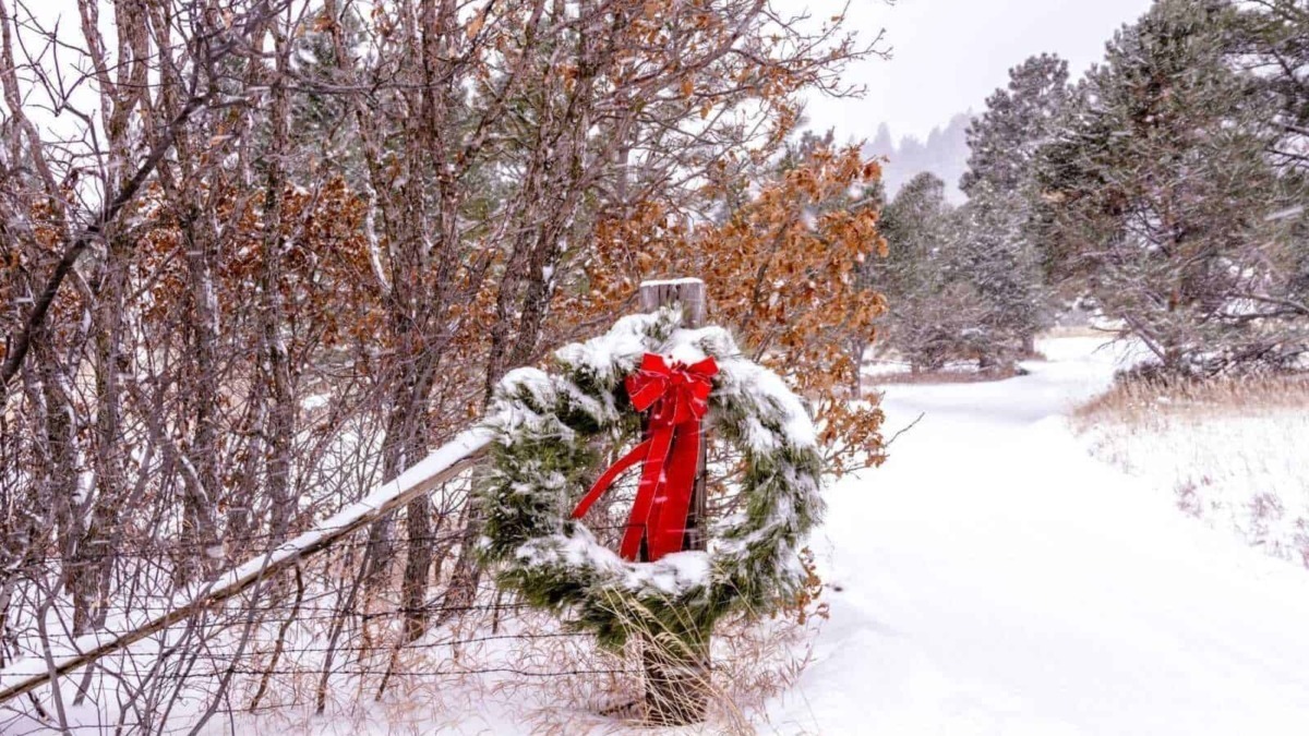 Neve sul sentiero di montagna con corona natalizia decorata con fiocco rosso in primo piano, ambiente invernale e paesaggio naturale, decorazioni natalizie, atmosfera festiva.