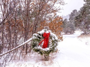 Neve sul sentiero di montagna con corona natalizia decorata con fiocco rosso in primo piano, ambiente invernale e paesaggio naturale, decorazioni natalizie, atmosfera festiva.