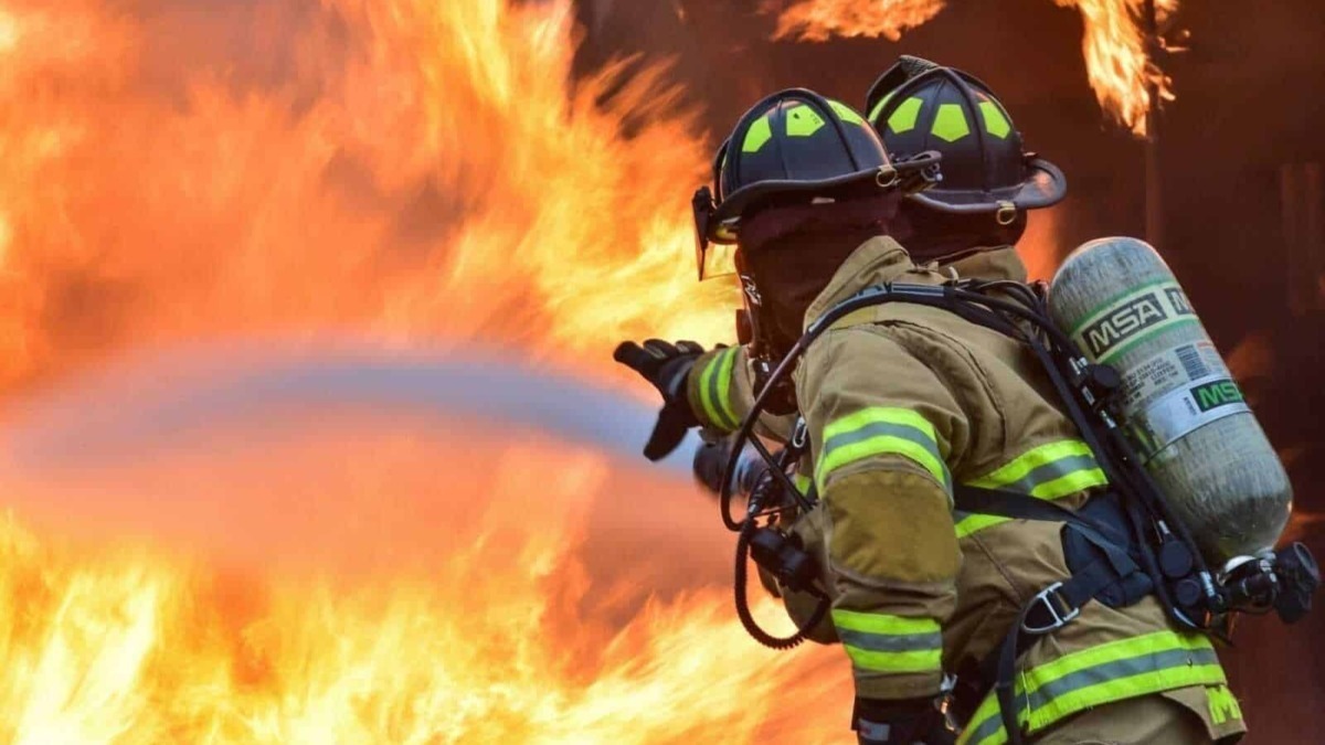 Sensan firefighting firefighter wearing protective gear and helmet extinguishing a blaze with a fire hose during a wildfire emergency.