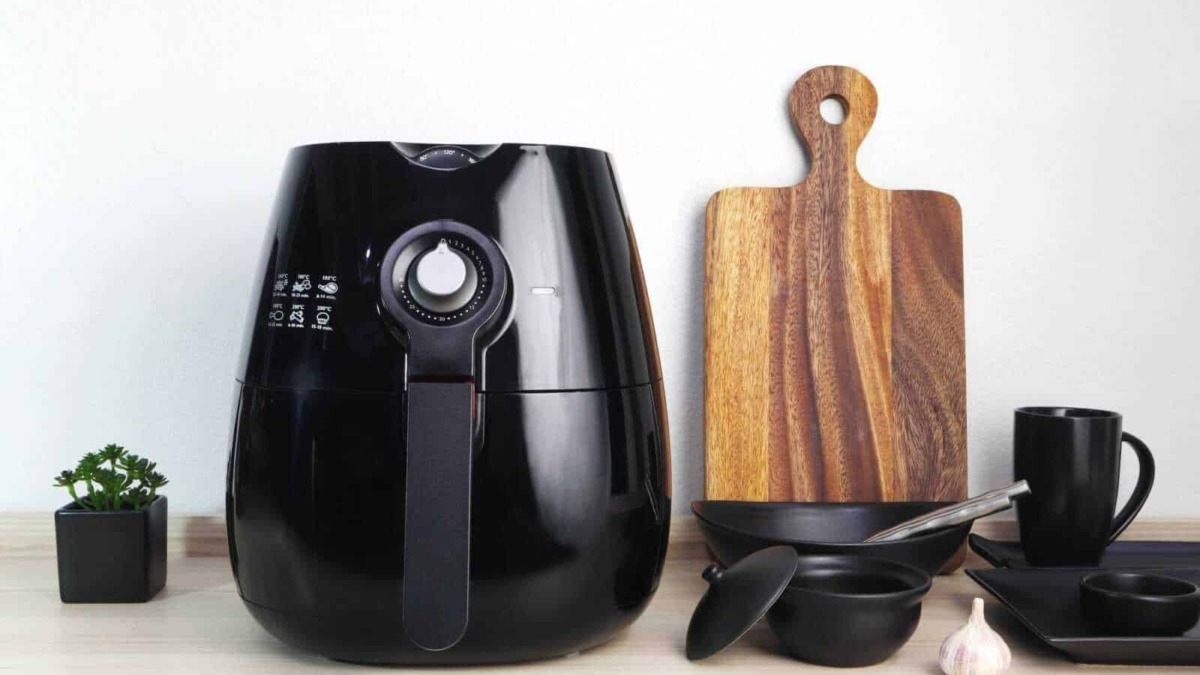 Velocità di cottura con friggitrice ad aria nera su cucina moderna, accessori di cucina eleganti con piante e spezie, stile minimalista e funzionale per ricette sane e veloci.