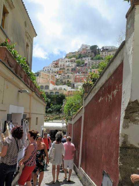 Passeggiata tra strette vie di Positano con case colorate sulla collina, panorama di mare e cielo azzurro sullo sfondo, atmosfera mediterranea, turismo, itinerario in Costiera Amalfitana.