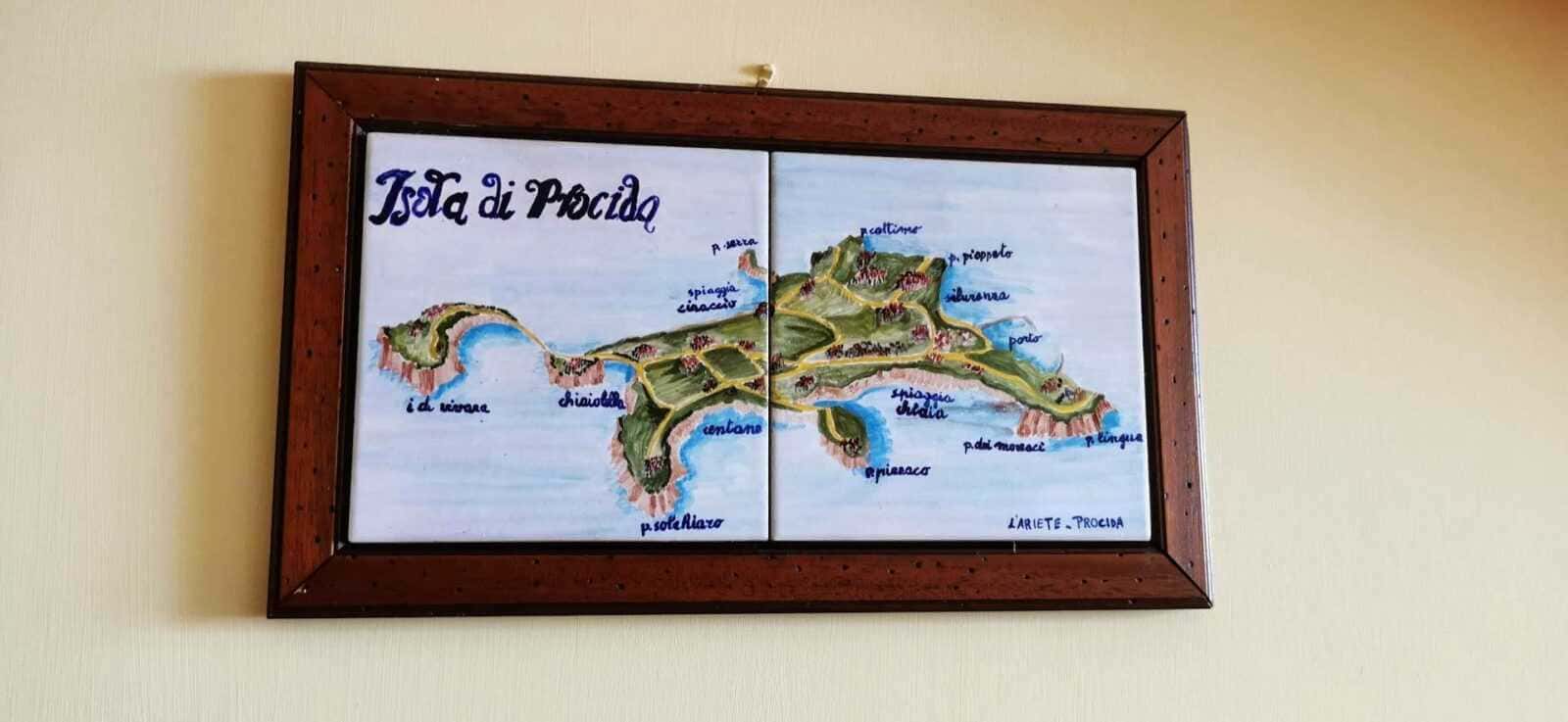 Colorful hand-painted map of the island of Procida, Italy, showing beaches, landmarks, and local areas, framed on a wall. Ideal for travel, tourism, and Italian island exploration content.