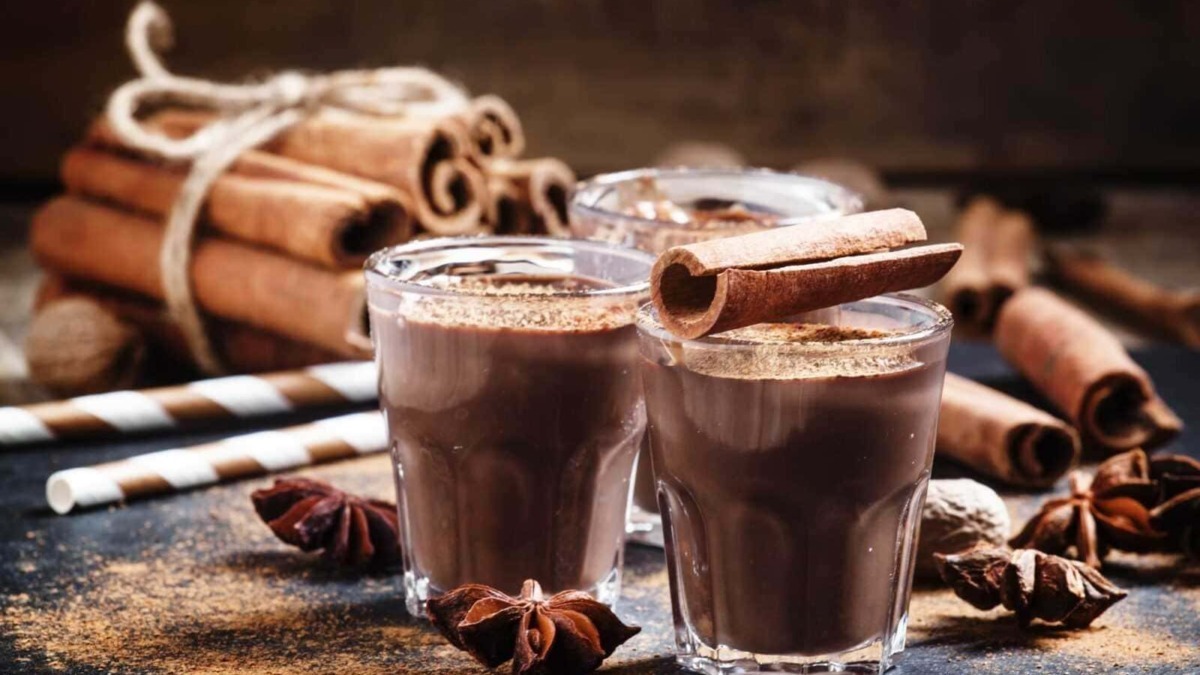 Deliziose cioccolate calde con cannella in bicchieri di vetro, accompagnate da bastoncini di cannella e spezie, perfette per le idee di ricette e dolci autunnali.